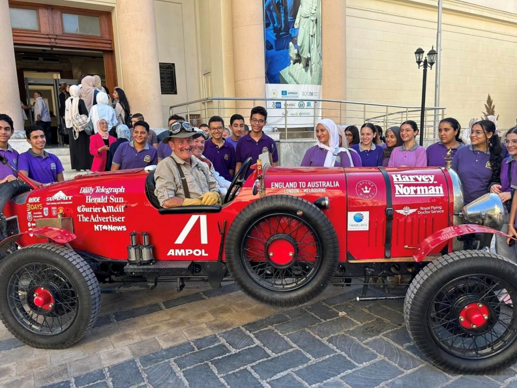 Matthew Benns, Editor-at-Large at Sydney’s The Daily Telegraph, and Warren Brown, an editorial cartoonist for the same outlet, sit inside a 1925 Bean model car, surrounded by admirers outside the Greco-Roman Museum in Alexandria, Egypt.